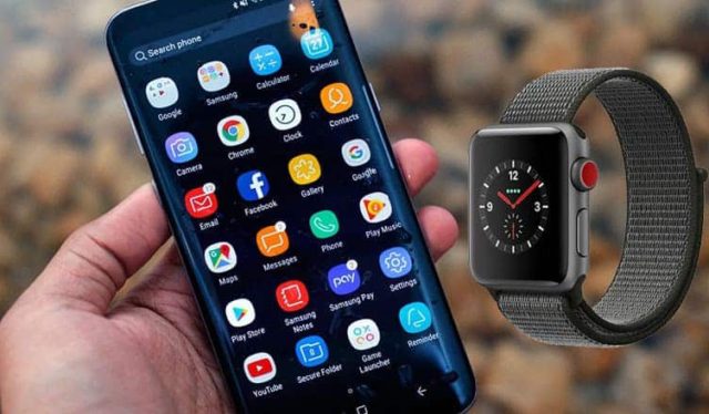 Από το iPhoneIslam.com, ένα άτομο κρατά ένα Apple Watch δίπλα σε ένα smartphone και αναρωτιέται για τη συμβατότητα με συσκευές Android.