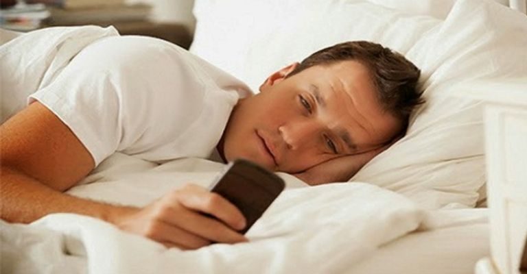 iPhoneMuslim.com से, एक आदमी अपने iPhone का उपयोग करते हुए बिस्तर पर लेटा हुआ है।
