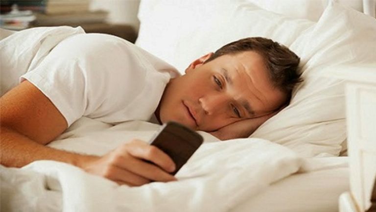 من iPhoneIslam.com، رجل يرقد في السرير مستخدما هاتفه الآيفون.