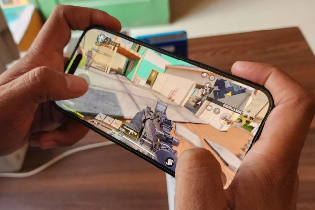 iPhoneMuslim.com से, एक व्यक्ति iPhone 15 Pro सुविधाओं वाले फ़ोन पर वीडियो गेम खेलता है।