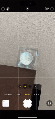 از iPhoneIslam.com، آیفونی که تصویر یک سکه را روی میز نشان می دهد، 18 ویژگی پنهان جدید را در برنامه دوربین iOS 17 به نمایش می گذارد.