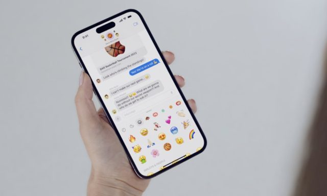 iPhoneIslam.com'da bir kadın, üzerinde emojiler ve yeni özellikler bulunan bir iPhone tutuyor.