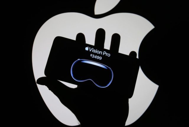 Mula sa iPhoneIslam.com, Hawak ng isang empleyado ang isang Apple phone sa harap ng logo ng Apple habang nagsasanay sa Apple.