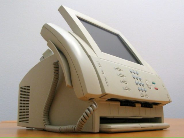 Van iPhoneIslam.com, een faxapparaat met hoorn, bedieningspaneel en Apple-logo op bureau.