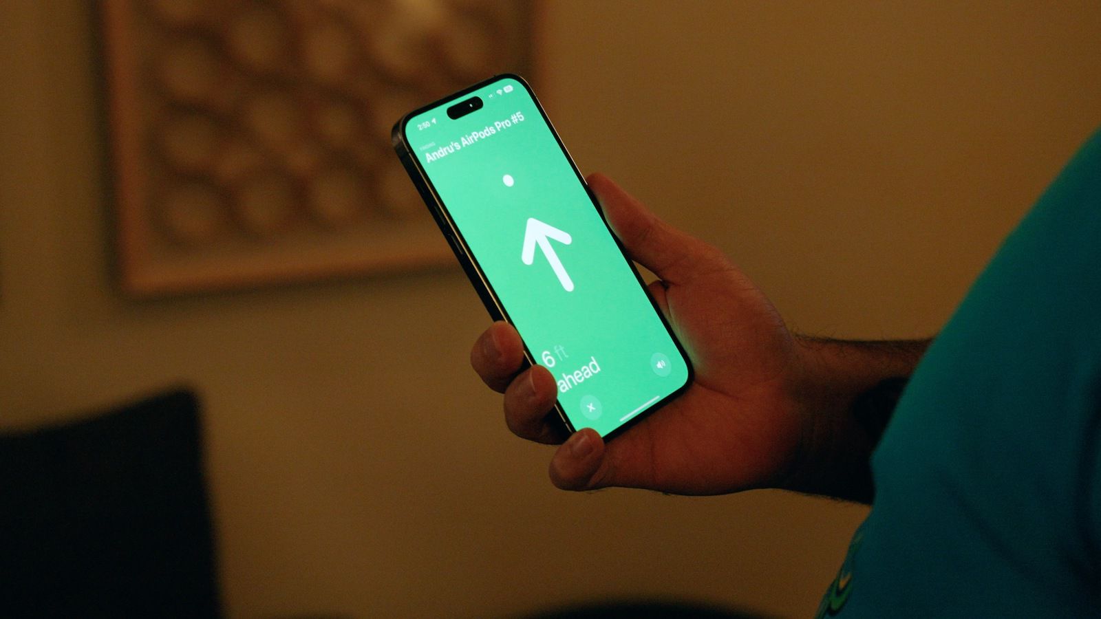من iPhoneIslam.com، شخص يحمل هاتفًا ذكيًا ويعرض تطبيق ملاحة مع سهم يشير إلى الاتجاه ويرتدي سماعات AirPods.