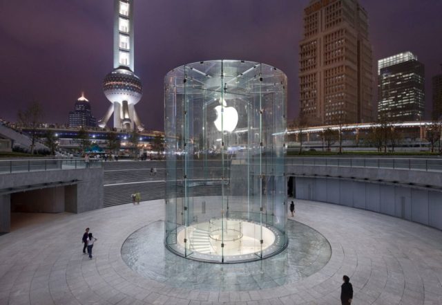 Von iPhoneIslam.com steht ein gläserner Apfelladen in einer städtischen Abendkulisse mit dem leuchtenden Oriental Pearl Tower im Hintergrund und symbolisiert ein atemberaubendes visuelles Zeugnis dessen, was zwischen August passiert