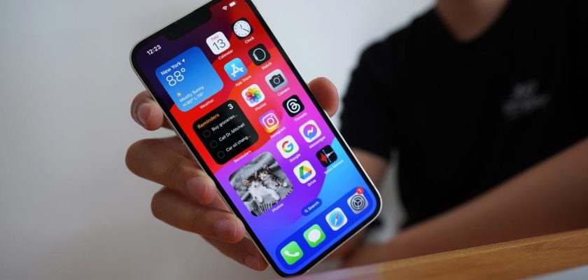 С сайта iPhoneIslam.com: Человек держит iPhone и отображает на экране красочные значки приложений, при этом устройство находится в фокусе на размытом фоне.