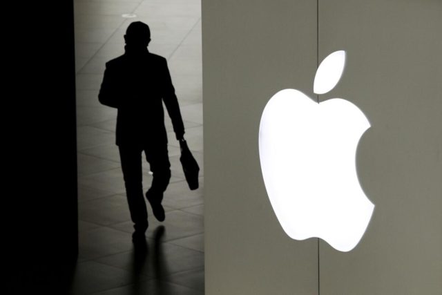 iPhoneIslam.com에서, Vision Pro 안경을 사용하여 조명이 켜진 사과 로고 옆을 걷고 있는 사람의 실루엣.