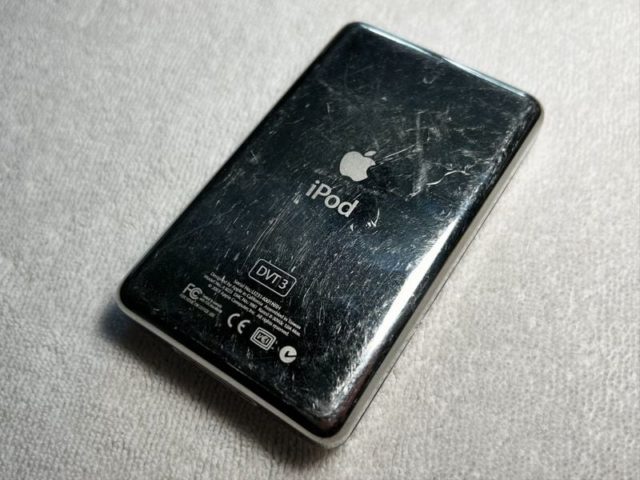 من iPhoneIslam.com، جهاز iPod أسود مخدوش ومخدوش عليه شعار Apple ونص "iPod" على ظهره، موضوع على سطح مزخرف، يبدو كما لو أنه شهد أيامًا أفضل في مايو.