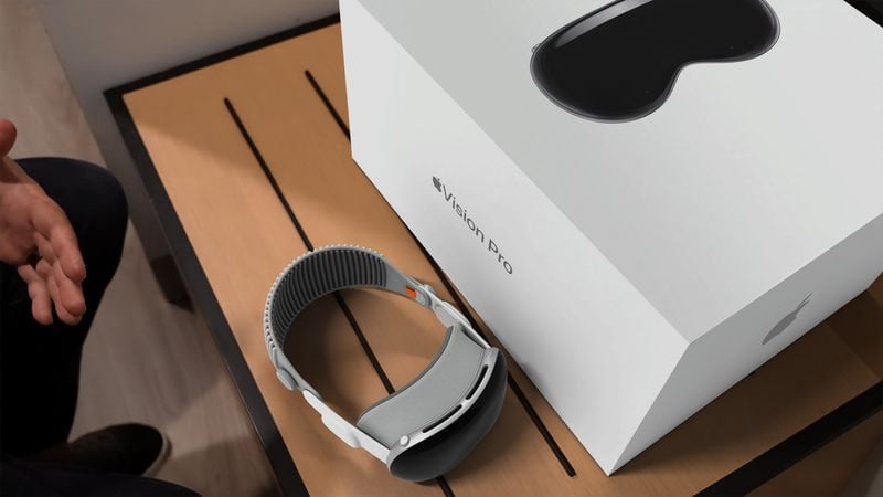 From iPhoneIslam.com 가상 현실 안경 한 쌍과 Apple Vision Pro 상자가 나무 표면 위에 놓여 있고 프레임에 사람의 손이 부분적으로 보입니다. 마치 자연 환경에서 최신 뉴스 기술을 포착하는 것처럼 보입니다.