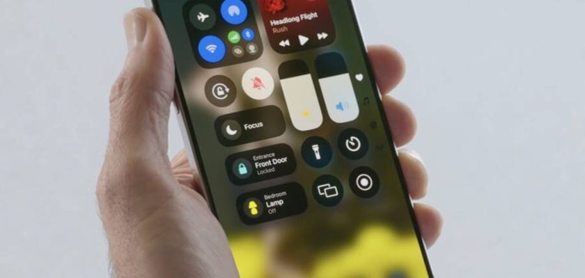 iPhoneIslam.com より、スマートフォンを持つ手は、iOS 18 のコントロール センターを示しています。このコントロール センターには、Wi-Fi、Bluetooth、輝度制御、文字起こしを容易にするメディア再生オプションなどのさまざまなクイック設定が備わっています。