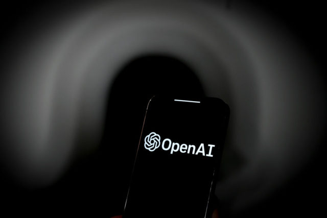 من iPhoneIslam.com، شاشة هاتف ذكي تعرض شعار OpenAI على خلفية داكنة غير واضحة، تذكرنا بعنوان رئيسي في أخبار مايو.