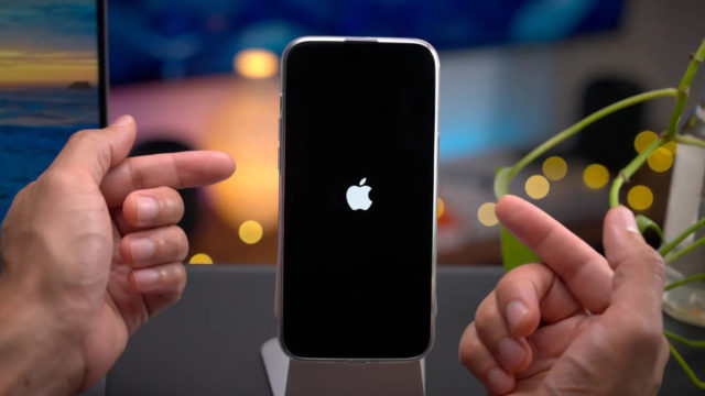 De iPhoneIslam.com Un par de manos apuntan hacia un iPhone que está parado en la acera. La pantalla del iPhone, que brilla con el logotipo de Apple sobre un fondo negro, resalta su elegante diseño incluso antes de que sea necesario reparar una grieta en la visión del futuro.