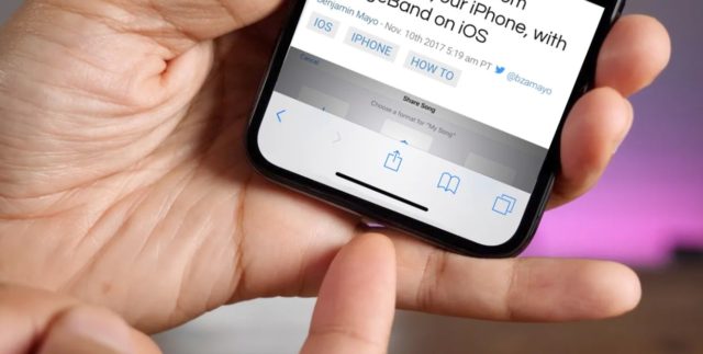 Dari iPhoneIslam.com, gambar close-up tangan seseorang yang memegang iPhone dan melihat halaman web. Tangan orang tersebut yang lain menunjuk ke arah indikator beranda yang terletak di bagian bawah layar iPhone, menunjukkan target rahasia yang mungkin ingin mereka ketahui.