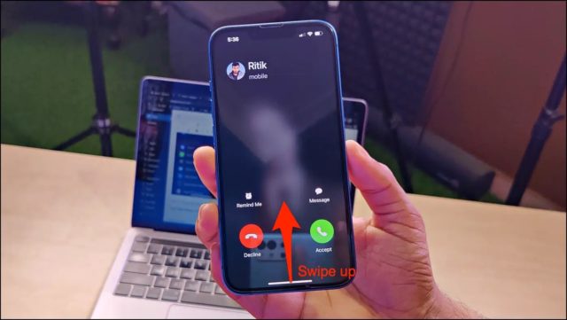 من iPhoneIslam.com، يد تحمل جهاز iPhone تظهر مكالمة واردة من "Ritik" مع خيارات للرفض، وتذكيري، والرسالة، والقبول. تعرض الشاشة سهمًا أحمر يشير إلى الأعلى مع النص "اسحب لأعلى". للتحكم السريع، يمكنك أيضًا استخدام زر الباور لإنهاء المكالمات بسرعة.