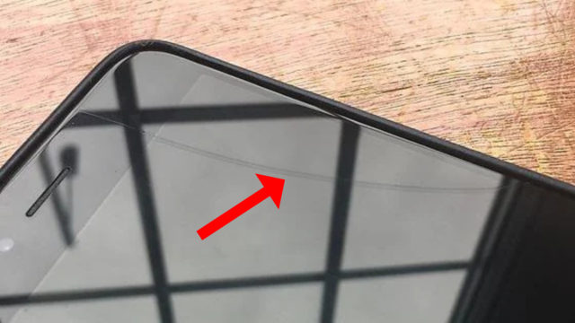 Da iPhoneIslam.com, un primo piano dello schermo di uno smartphone con una crepa evidente, indicata da una freccia rossa. Lo schermo del telefono mostra anche il riflesso della rete della finestra, confermando la necessità di riparare la crepa dell'Arri-Phone.