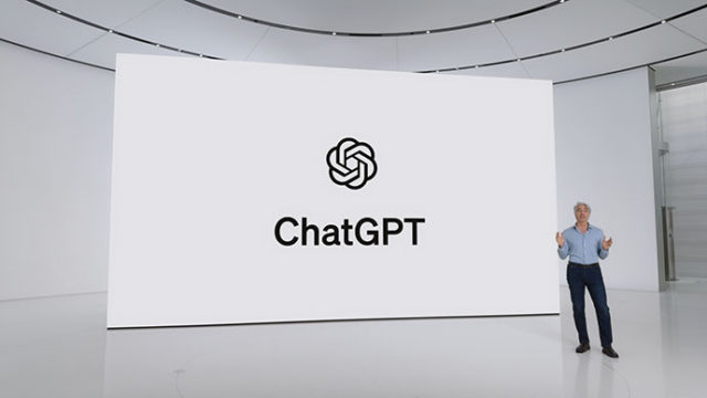 من iPhoneIslam.com، يقف شخص على خشبة المسرح أمام شاشة كبيرة تعرض شعار ChatGPT واسمه. يبدو أن المكان عبارة عن غرفة عرض حديثة وبسيطة.
