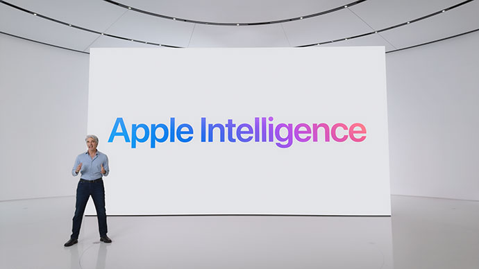 من iPhoneIslam.com، شخص يقف على خشبة المسرح أمام شاشة كبيرة يعرض نص "Apple Intelligence" باللونين الأزرق والوردي المتدرجين.