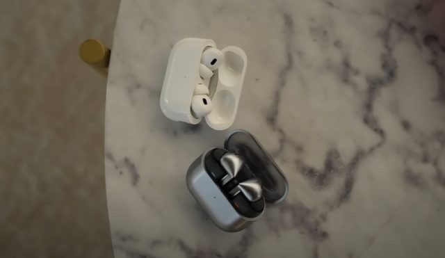 Z iPhoneIslam.com Para białych słuchawek AirPods Pro 2 w otwartym białym etui ładującym i para srebrnych słuchawek dousznych w otwartym srebrnym etui ładującym leżą na marmurowym stole.