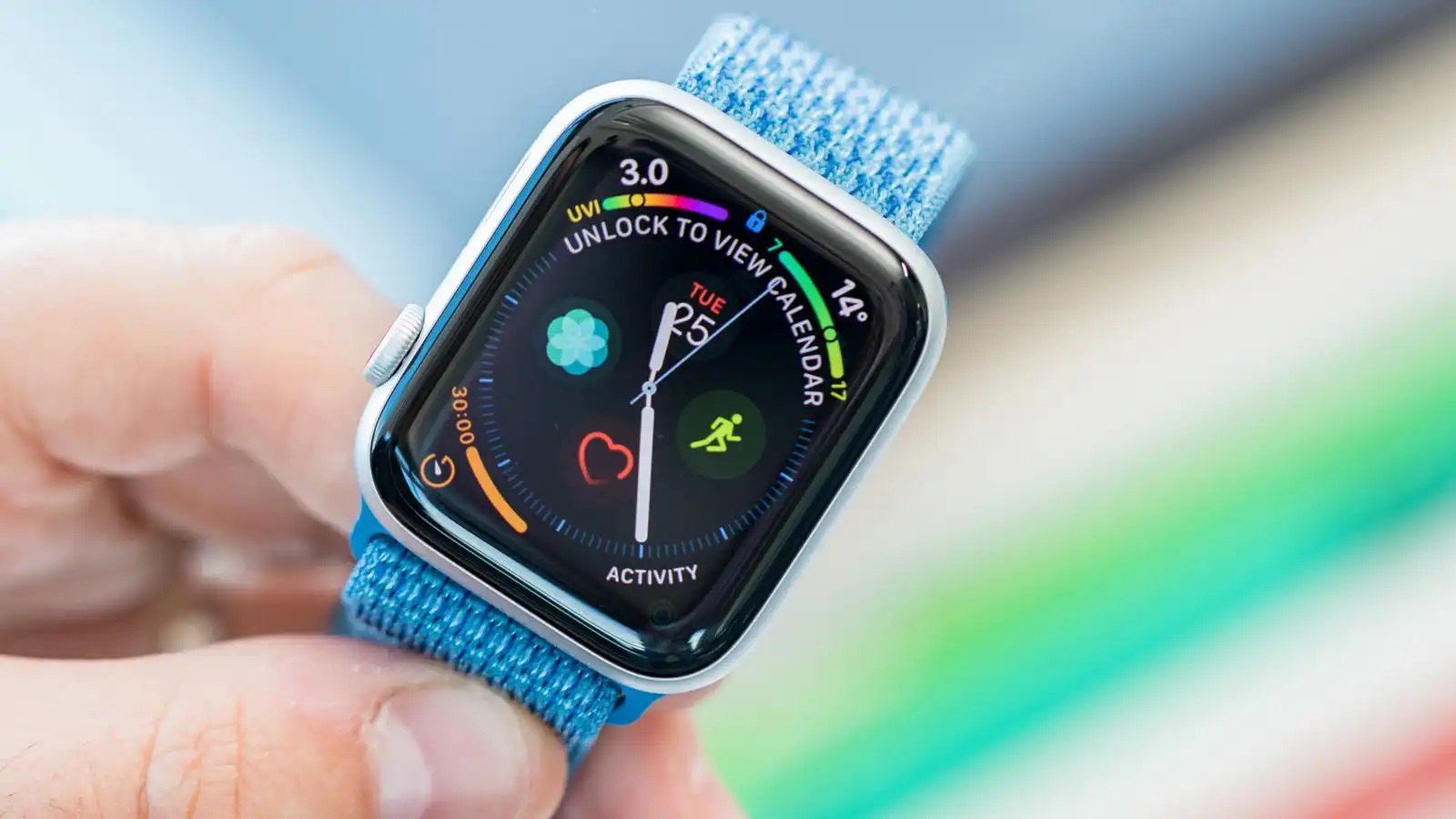 من iPhoneIslam.com، صورة مقربة لساعة آبل القديمة بحزام من القماش الأزرق. تعرض الشاشة أيقونات تطبيقات مختلفة، وإشعارات التقويم، ومعلومات الطقس، ومقاييس النشاط البدني.