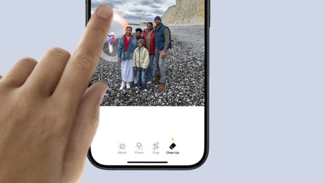 From iPhoneIslam.com, A person uses the Cleanup tool in the Photos app on iOS 18 to remove part of a group photo taken on a rocky beach.