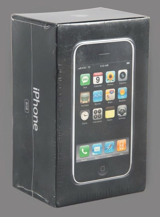 From iPhoneIslam.com, a sealed box of the original iPhone 2G on a gray background, showing the front and side view of the packaging, perfect for tech enthusiasts who follow news on the sidelines.