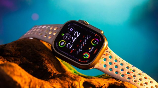 Da iPhoneIslam.com, uno smartwatch con cinturino bianco traforato, che indica l'ora alle 2:42 e una varietà di widget, appoggiato su una roccia su sfondo blu sfumato. Questa edizione in edizione limitata celebra il decimo anniversario dell'iconico Apple Watch