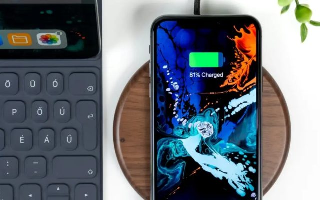 Van iPhoneIslam.com toont een smartphone met iOS 18 een batterijlading van 81%, wordt deze op een draadloos oplaadpad naast het toetsenbord geplaatst en worden de oplaadopties voor de iPhone-batterij weergegeven.