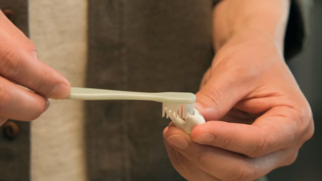 Desde iPhoneIslam.com, una persona sostiene un cepillo de dientes de color verde claro y aplica pasta de dientes a las cerdas para garantizar una limpieza eficaz de los dientes. Cerca de allí, los AirPods de Apple están listos para el día siguiente.