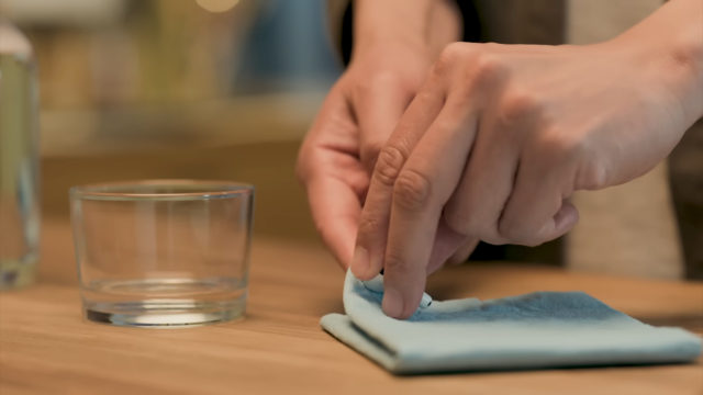 Desde iPhoneIslam.com, Hands dobla con cuidado un paño azul junto a una taza vacía sobre una superficie de madera, preparándose para limpiar los AirPods.