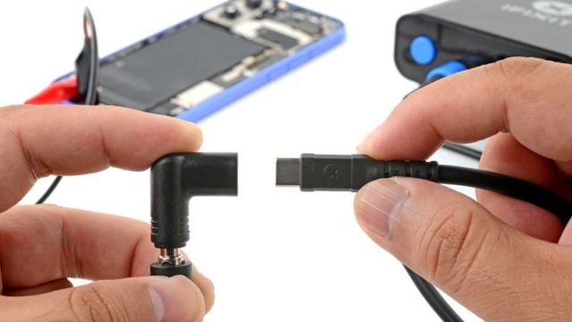 来自 iPhoneIslam.com，两只手握住直角电源连接器和 USB-C 电缆，准备在后台为打开的设备充电。在准备过程中，十月新闻的低语在空气中萦绕。