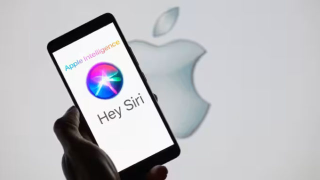 من iPhoneIslam.com، هاتف ذكي يعرض عبارة "Hey Siri" مع شعار Apple Intelligence، محمولاً بيد أمام خلفية ضبابية تحتوي على شعار Apple.