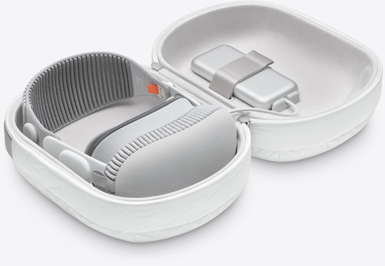 من iPhoneIslam.com، جهاز عصابة رأس إلكترونية باللونين الرمادي والأبيض، يشبه في تصميمه نظارة آبل فيجن برو، مع الملحقات، يتم تخزينه بدقة في حقيبة حمل مبطنة مفتوحة.