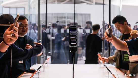 من موقع فون إسلام: أشخاص يلتقطون صورًا لهاتف ذكي قابل للطي معروض على منصة في إحدى الفعاليات التقنية، بينما يناقش الجمهور سبب الشعبية الكبيرة لهاتف ذكي قابل للطي في الخلفية.