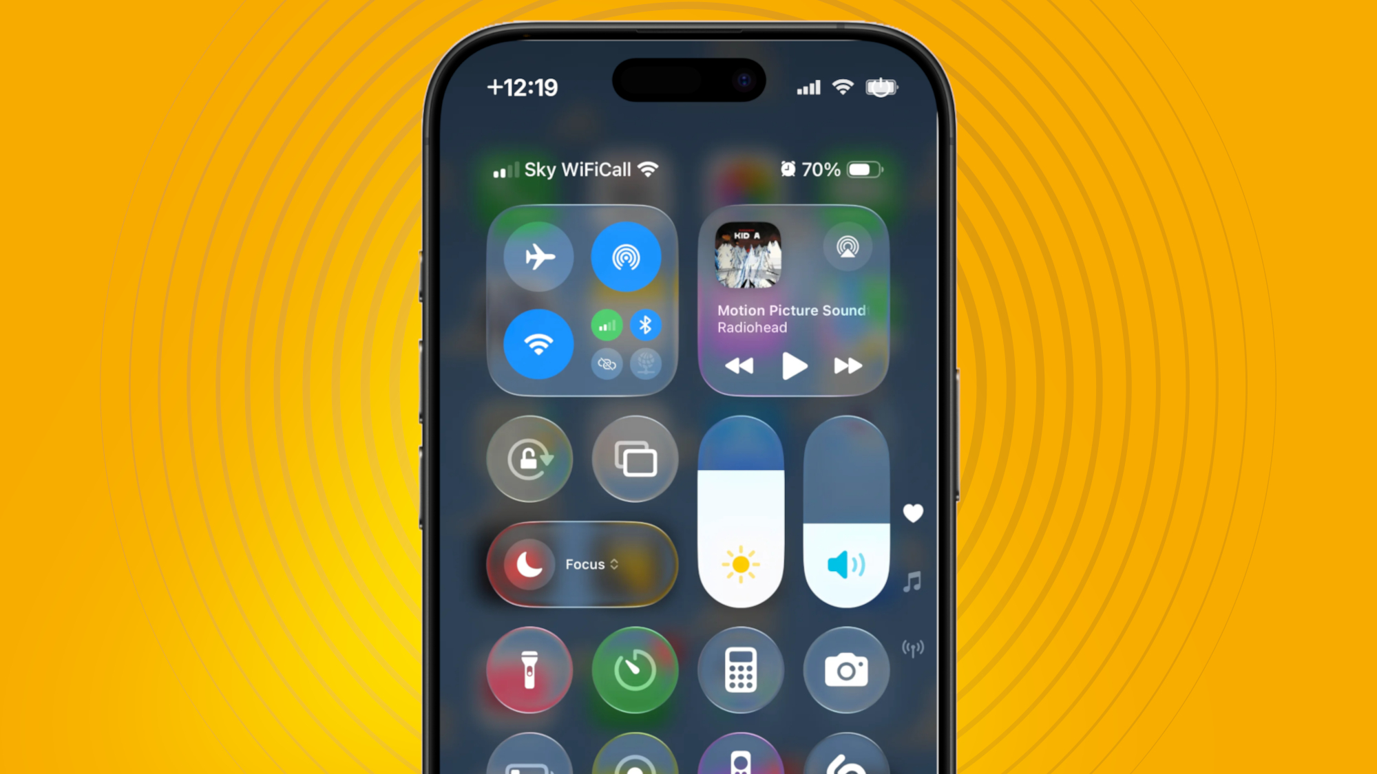 من موقع فون إسلام: تعرض شاشة iPhone مركز التحكم مع العديد من الأيقونات وعناصر التحكم على خلفية صفراء على شكل دائرة صفراء متحدة المركز، مع تسليط الضوء على ميزات iOS 26 مثل تقليل شفافية لتحسين الوضوح.