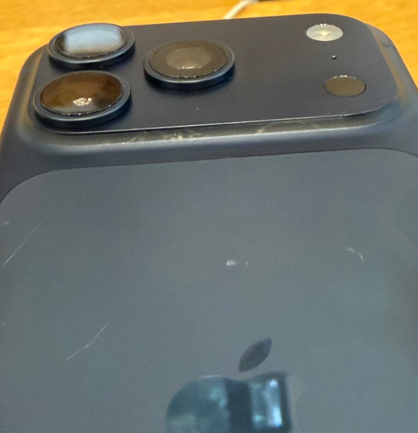 من موقع فون إسلام: صورة مقرّبة للجزء الخلفي من هاتف ذكي داكن اللون، ربما يشبه آي-فون 17، يظهر فيه ثلاث كاميرات خلفية وفلاش ولطخات سطحية مرئية - وهي مشكلة تصميم لاحظها بعض المستخدمين.