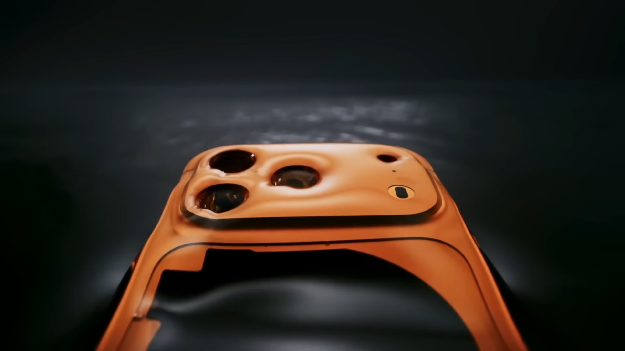 من موقع فون إسلام: منظر عن قرب لإطار هاتف ذكي برتقالي مشوه ومتموج باللون البرتقالي مع فتحتين للكاميرا وفتحة فلاش، على خلفية داكنة تبرز أخطاء آبل في تصميم الجهاز.