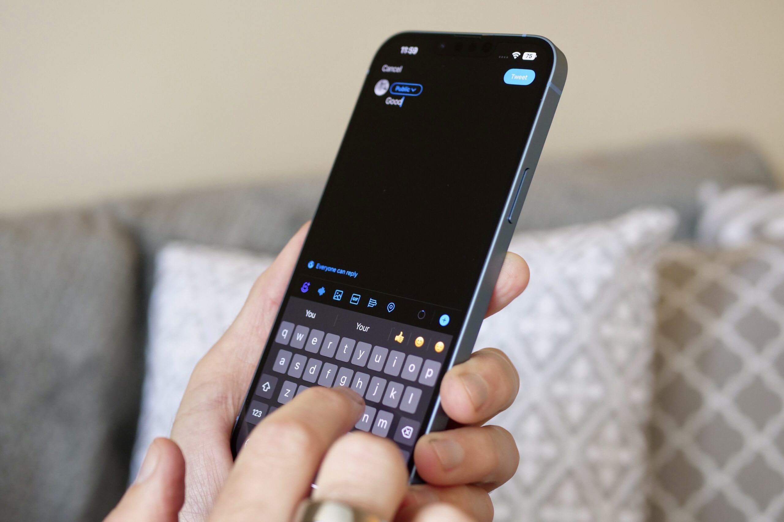 من موقع فون إسلام: شخص يكتب تغريدة عن إحباط مستخدمي الآي فون على هاتف ذكي بواجهة سوداء، ويجلس على أريكة ذات وسائد منقوشة في الخلفية.