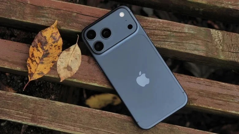 من موقع فون إسلام: يوضع على سطح خشبي بجانب ورقتين مجففتين باللون الأزرق الداكن آي-فون 17 مع ثلاث عدسات كاميرا ترمز إلى الأناقة وتذكر المستخدمين أحيانًا بمشكلة آي-فون مثل مشكلة الاتصال.