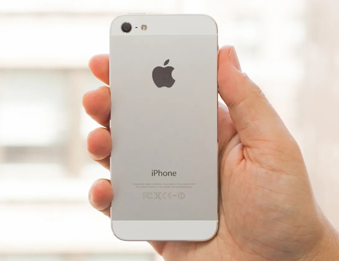 من موقع فون إسلام: يد تحمل هاتف آي فون إير فضي أنيق باللون الفضي يظهر من الخلف، ويظهر شعار أبل وكلمة "آيفون".