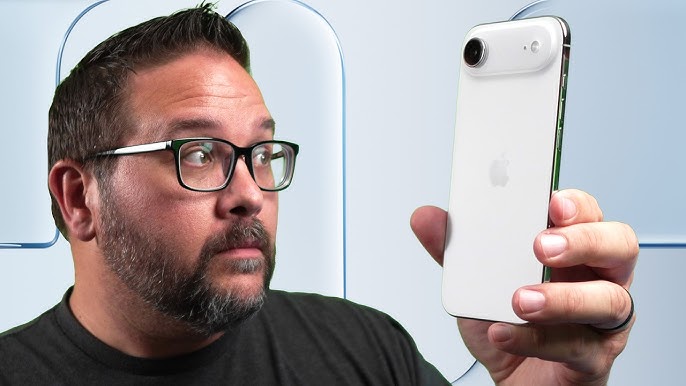 من موقع فون إسلام: رجل يرتدي نظارات ولحية ينظر إلى هاتف ذكي أبيض بعدسة كاميرا كبيرة، يفكر في أن يناسبك من ألوان آي فون، والهاتف مرفوع على خلفية فاتحة.