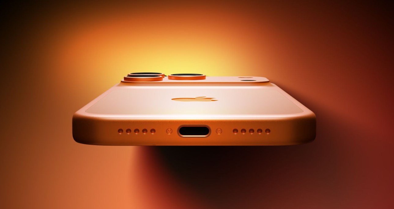 من موقع فون إسلام: لقطة مقرّبة لهاتف ذكي برتقالي اللون، من الأسفل، يظهر فيها منفذ USB-C، وفتحات مكبر الصوت، وكاميرات خلفية مزدوجة - تذكرنا بهاتف آي ماتس آي برو 18 الأخير - على خلفية برتقالية متدرجة.