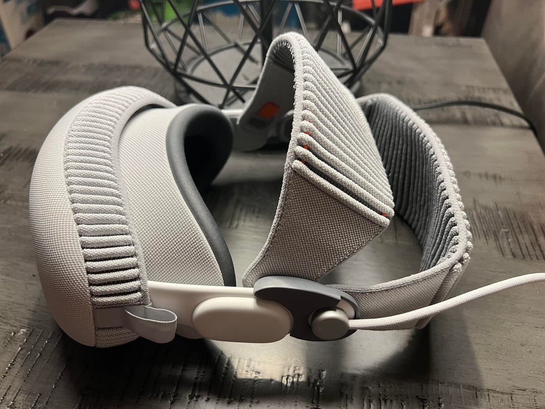 من موقع فون إسلام: صورة مقرّبة لحزام رأس مبطن رمادي اللون، ربما لسماعة رأس واقع افتراضي, يستند على سطح خشبي داكن مع قطعة معدنية مزخرفة في الخلفية - وهي مثالية لملخص الأخبار في أخبار التقنية وأحدث أخبار الأسبوع.