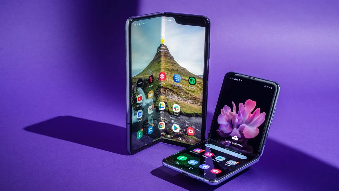 من موقع فون إسلام: يتم عرض هاتفين ذكيين قابلين للطي، يشبهان هاتفين ذكيين قابلين للطي على خلفية أرجوانية - أحدهما غير مطوي بالكامل مع خلفية جبلية، والآخر مطوي جزئياً.