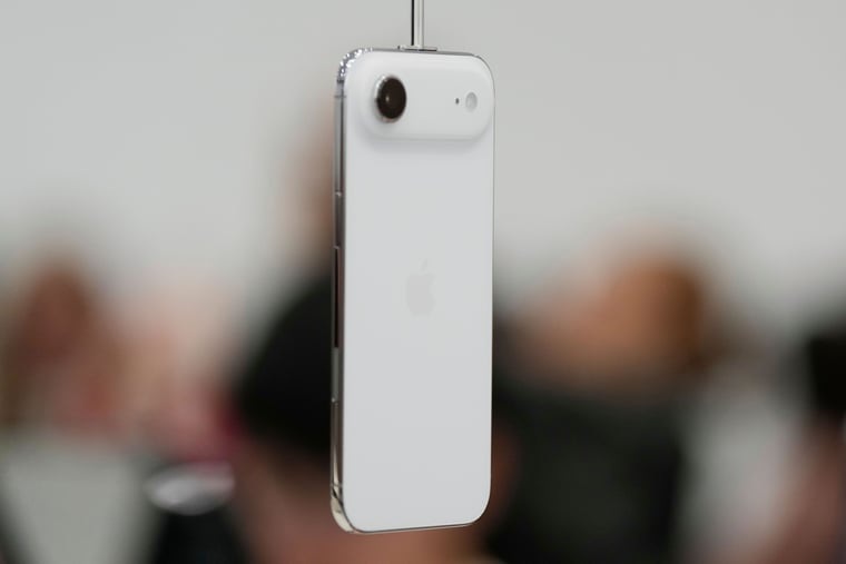 من موقع فون إسلام: تم تعليق كاميرا آي-فون إير 2 بيضاء اللون عمودياً في الهواء، حيث يظهر جانبها الخلفي والكاميرا على خلفية ضبابية.