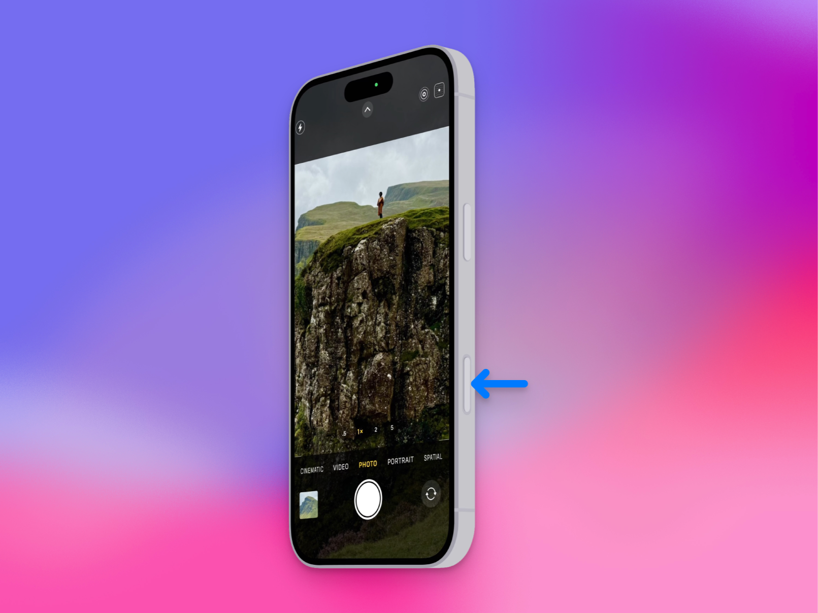 من موقع فون إسلام: يعرض الهاتف الذكي تطبيق كاميرا مع مشهد أفقي؛ يشير سهم أزرق إلى الزر الجانبي على الآي فون-يفون، مبرزا إحدى ميزات الذكاء الاصطناعي في التقاط الصور.