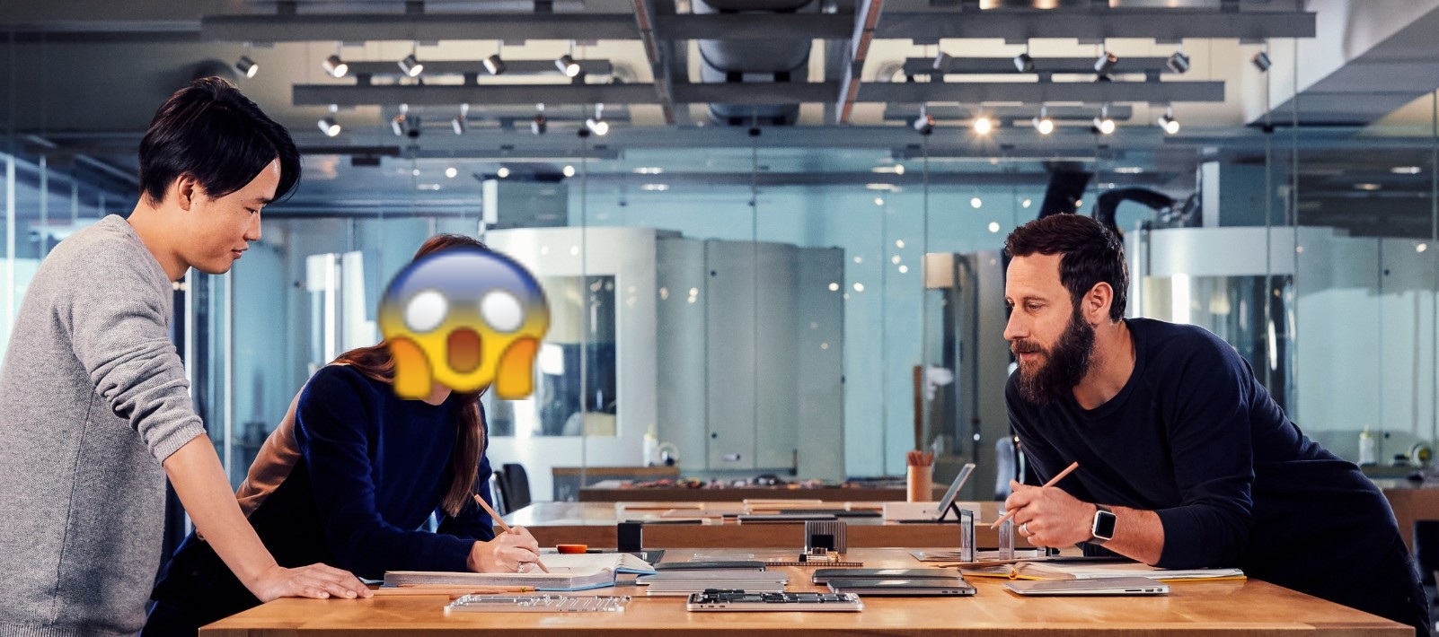 من موقع فون إسلام: ثلاثة أشخاص يعملون على طاولة في مكتب عصري مستوحى من آبل؛ وجه أحدهم مغطى برمز تعبيري لوجه مصدوم يمزج بين التصميم السلس وعدم الكشف عن هويته.