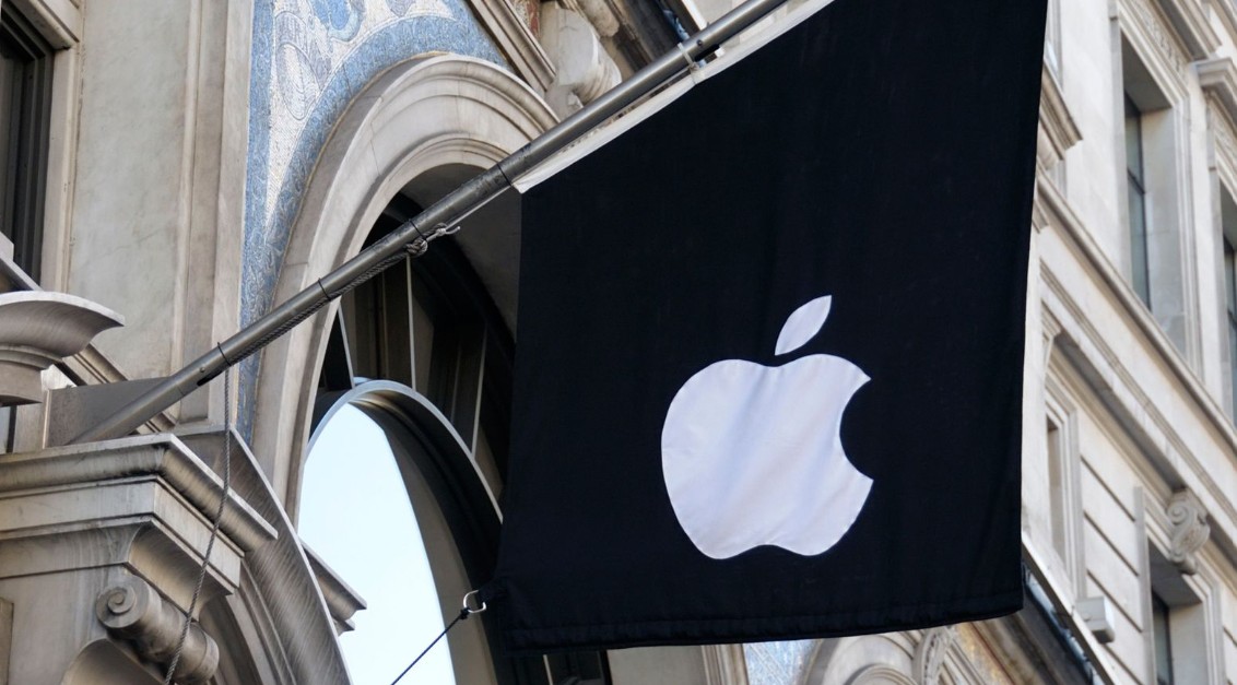 من موقع فون إسلام: علم أسود يحمل شعار آبل الأبيض معلق خارج مبنى ذي نوافذ مقوسة وتفاصيل معمارية مزخرفة، مما يعكس وجود آبل الصين.