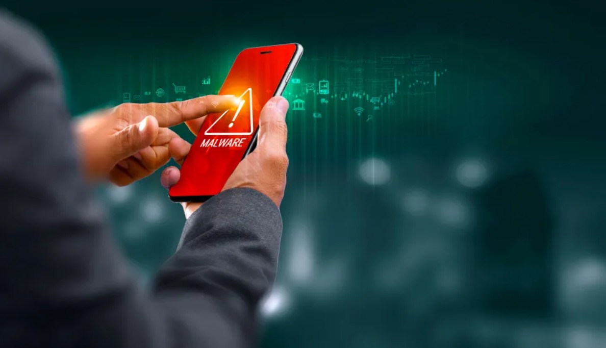 Van PhoneIslam: Een persoon die een smartphone vasthoudt, toont een waarschuwingssymbool voor malware op het scherm, wat wijst op een veiligheidsdreiging te midden van oplopende spanningen na een terroristische aanslag.
