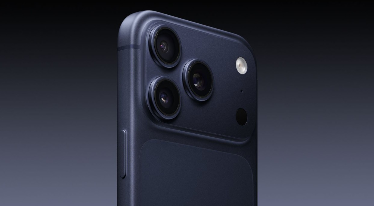 من موقع فون إسلام: لقطة مقرّبة لظهر آي-فون 17 بروبلو داكن اللون، تظهر ثلاث عدسات كاميرا وفلاش وزر على الجانب على خلفية سوداء - استكشف تفاصيل التصميم وابقَ على اطلاع على مشاكل الشحن.